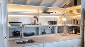 Une cuisine moderne avec des meubles blancs, un évier en acier inoxydable et divers ustensiles de cuisine rangés sur des étagères ouvertes.