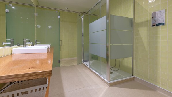 A modern bathroom with a wooden vanity, a glass shower enclosure, and green tiled walls.