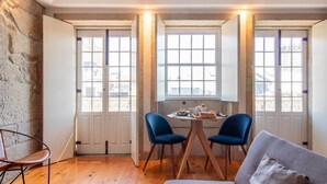 Un coin repas avec une table dressée pour deux personnes, deux chaises bleues et une vue sur la ville grâce à de grandes fenêtres.