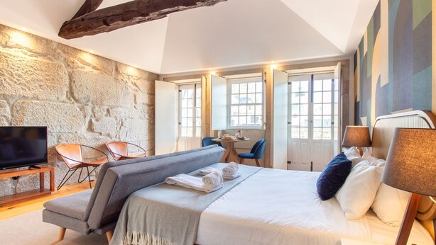 Une chambre d’hôtel moderne avec un mur en pierre, un grand lit avec des oreillers, une télévision, un canapé et un coin repas avec des chaises.