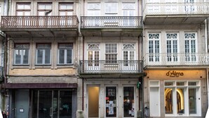 A row of multi-story buildings with balconies, a restaurant named 'd'Alma' on the right, and a visible entrance with a door and windows. - Allderman Apartment - Almada 3º F by LovelyStay (Porto)