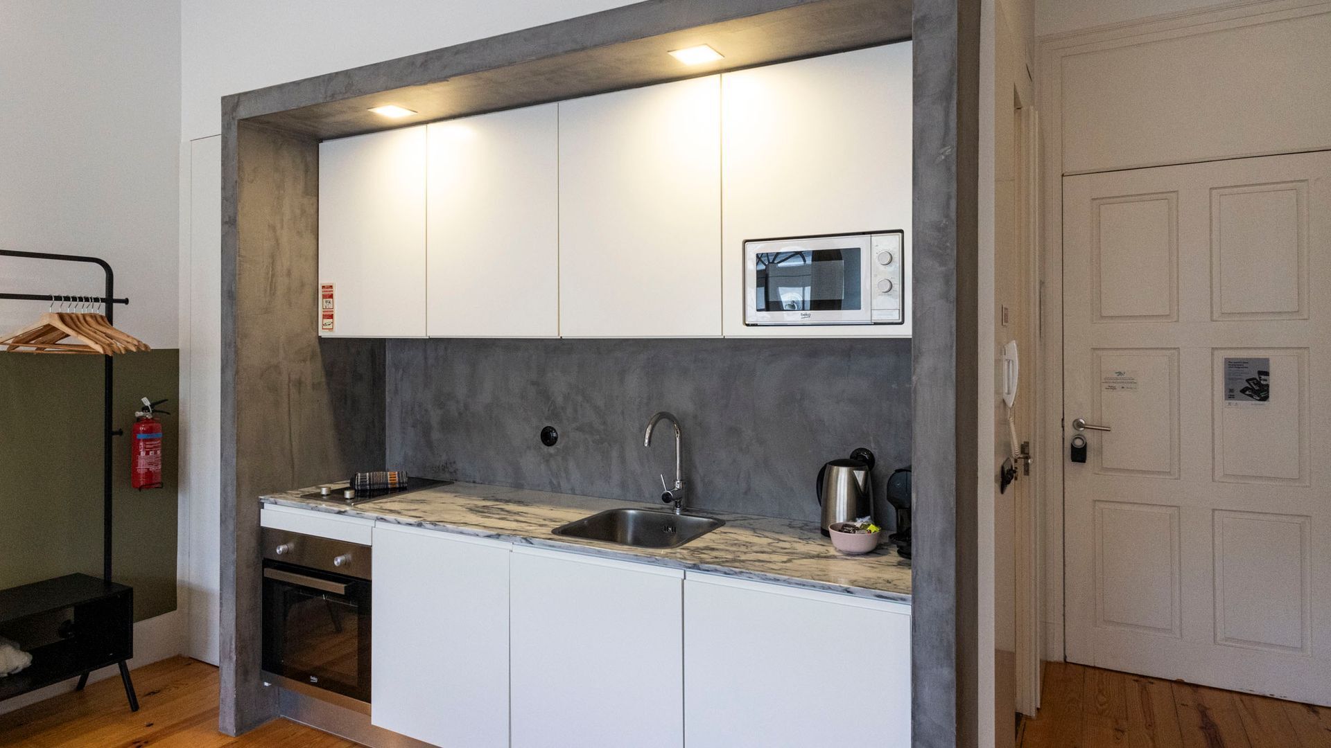 Una cucina compatta con mobili bianchi, un lavello in acciaio inossidabile, un forno a microonde e un piccolo forno.