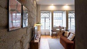 A cozy living room with a stone wall, a wooden coffee table, a brown sofa, and a lamp. - Allderman Apartment - Almada 3º F by LovelyStay (Porto)