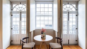 A room with a round table and two chairs, a bottle of wine, and a vase with pink flowers. - Allderman Apartment - Almada 3º F by LovelyStay (Porto)