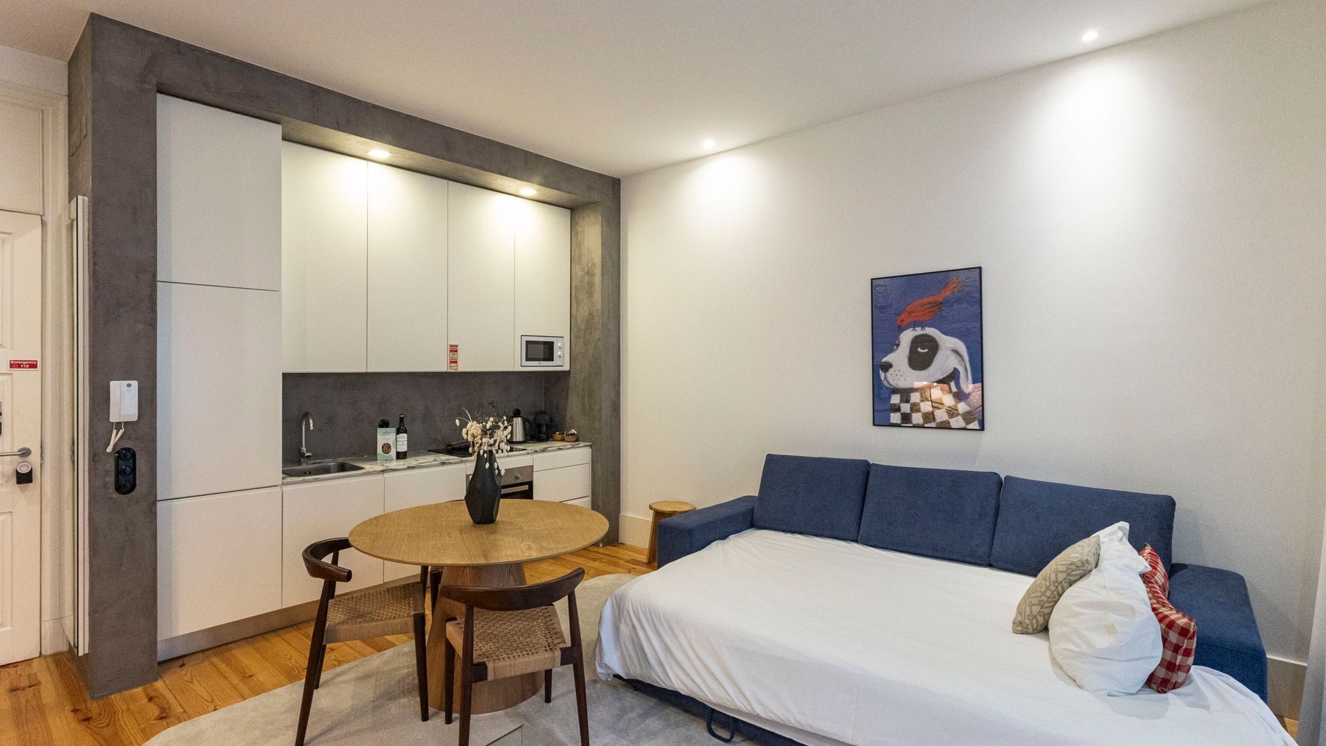 A compact bedroom with a bed, a small table, and a kitchenette.