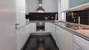 Una cucina moderna con mobili bianchi, un forno in acciaio inossidabile, una lavastoviglie e un pannello schienrale rivestito in piastrelle nere.