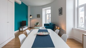 Un soggiorno moderno con un ampio tavolo da pranzo, una parete di colore verde acqua e vista sulla città attraverso grandi finestre.