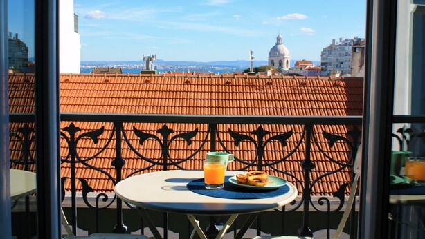 Un balcone con un tavolo apparecchiato per la colazione, con un bicchiere di succo d'arancia e pasticcini.