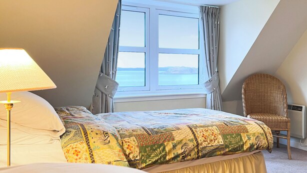 A bedroom with a bed, a chair, a lamp, and a window with a view of the sea. - 3 bedroom accommodation in Arnisdale, Kyle of Lochalsh (Arnisdale, Kyle of Lochalsh)