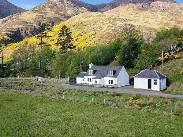 A rural setting with a white house, a smaller white structure, and a mountain backdrop.