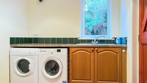A laundry room with a washing machine, dryer, wooden cabinets, a window with a view, and a tiled backsplash. - 3 bedroom accommodation in Arnisdale, Kyle of Lochalsh (Arnisdale, Kyle of Lochalsh)