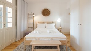 A minimalist bedroom with a wooden bed, a bedside table, a small round rug, and a ladder against the wall.