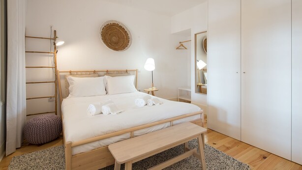 Een keurig opgemaakt slaapkamer met een bed, nachtkastje, lamp en een hangmand.