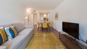 A modern living room with a sofa, a TV, and a dining area with chairs and a table.