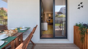 A modern outdoor dining area with a wooden table and chairs, a breakfast setup, and a view into the interior through a glass door.