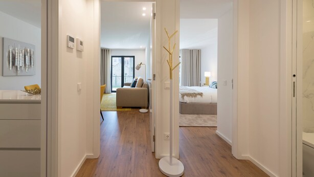 A modern hotel room with a wooden floor, a sofa, a bed, and a view of the city through large windows.