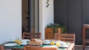 A breakfast table set with plates, glasses, and a basket of bread, with chairs around it.
