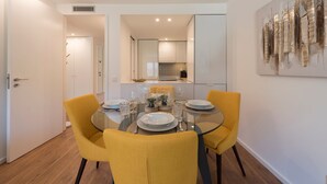 A dining area with a glass table, yellow chairs, and a modern kitchen in the background.