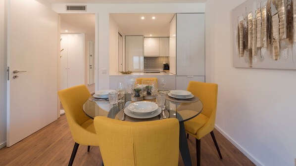 A dining area with a glass table, yellow chairs, and a modern kitchen in the background.