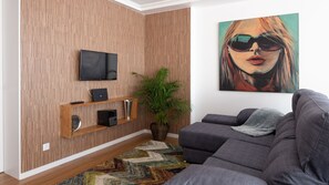 Un salon moderne avec un lambris en bois, un téléviseur à écran plat, un système audio, une plante en pot et un grand tableau abstrait.