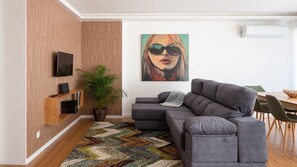 Un salon moderne avec un canapé gris, un mur d’accent en bois, un grand tableau, une plante en pot et un coin repas comprenant une table et des chaises en bois.