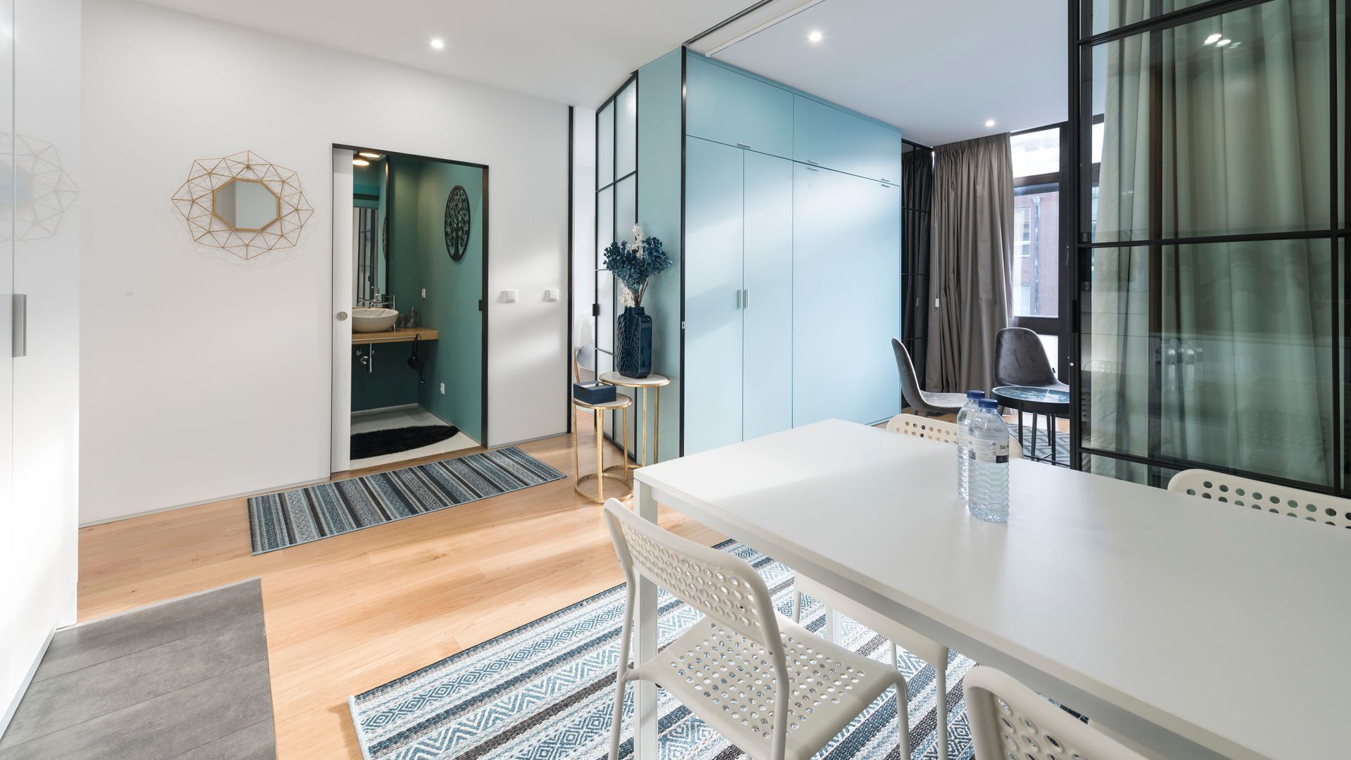 Une chambre d’hôtel moderne dotée d’une grande fenêtre, d’une table à manger blanche et d’un espace salle de bain séparé.