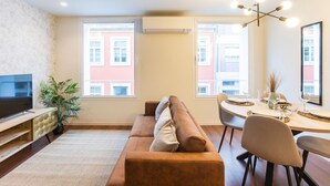 Ein modernes Wohnzimmer mit Sofa, Fernseher, Esstisch und Stühlen.