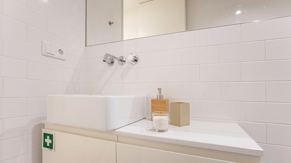 A bathroom with white tiles, a sink, a mirror, and a first aid kit. - Bombarda 1F - Cozy Studio by LovelyStay (Porto)
