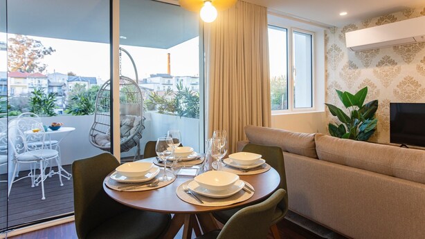 Ein modernes Wohnzimmer mit Essbereich, einer Couch, einem Fernseher und einem Balkon mit Hängesessel.