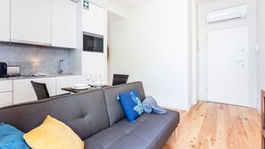 A modern living room with a grey sofa, a dining table, and a kitchen area with white cabinets and a microwave.