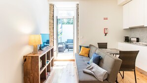 Un espacio habitable pequeño con sofá, televisor, estante de madera, mesa de comedor y zona de cocina.