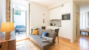 A compact living space with a sofa, a dining table, a kitchen area, and a view of the outdoors.