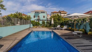 Una piscina con plataforma de madera, rodeada de vegetación y una cerca.