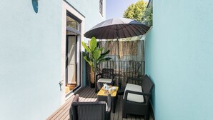 Un pequeño patio al aire libre con mobiliario de mimbre, una mesa lista para el desayuno y un paraguas grande que da sombra.