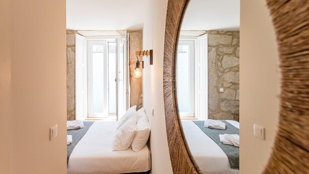 Un dormitorio con cama, espejo, lámpara y pared de piedra.