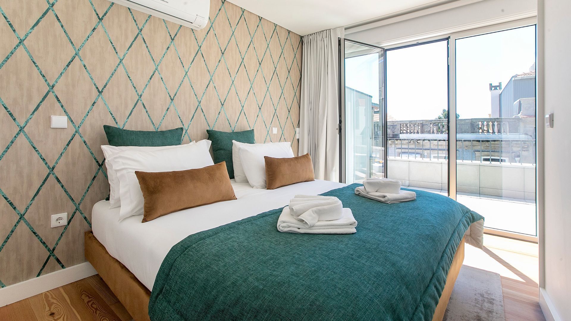 A hotel room with a large bed, a view of the city through a sliding glass door, and a patterned wall.
