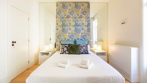A hotel room with a large bed, two bedside tables with lamps, a patterned curtain, and a small picture on the wall.