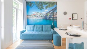 A modern living room with a blue sofa, a dining table with chairs, a striped rug, and a cityscape mural on the wall. - Porto Flores Plaza by LovelyStay (Porto)