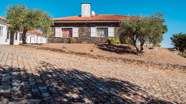 Un edificio de piedra con techo de tejas, camino de adoquinado y árboles circundantes.