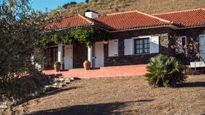 Una casa de piedra con techo de tejas rojas, contraventanas blancas y entrada de ladrillo.