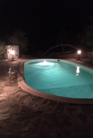 Una piscina nocturna con baldosas de piedra y dos luces.