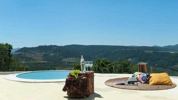 A poolside area with a view of rolling hills, a bottle of white wine, and a glass on a wooden stump. - Bee Moinho - One Bedroom House, Sleeps 3 (Mafra)