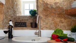A kitchen with a stone wall, a sink, a wine bottle, a glass, a potted plant, and a sign. - Bee Moinho - One Bedroom House, Sleeps 3 (Mafra)