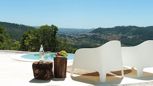 A poolside setting with a view of a valley, two white lounge chairs, a bottle of water, and a plate of grapes. - Bee Moinho - One Bedroom House, Sleeps 3 (Mafra)