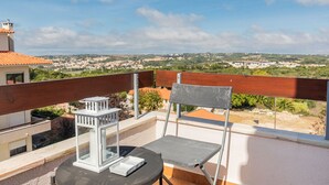Ein Balkon mit Blick auf eine Stadt, ein Stuhl, ein kleiner Tisch und eine Laterne.