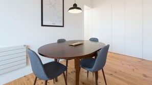 A round wooden table with four grey chairs, a black pendant light, and a framed map on the wall.