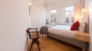 A bedroom with a bed, a chair, a bedside table, and a window.