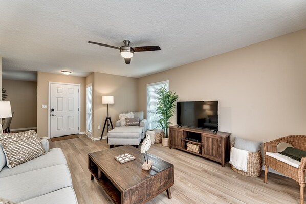 A living room with a sofa, coffee table, TV, and a ceiling fan. - The Nest at Quail Hollow (St. Augustine)