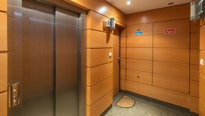 Un ascensor de hotel con puerta metálica, panel de control con flechas direccionales y un felpudo en la parte inferior.