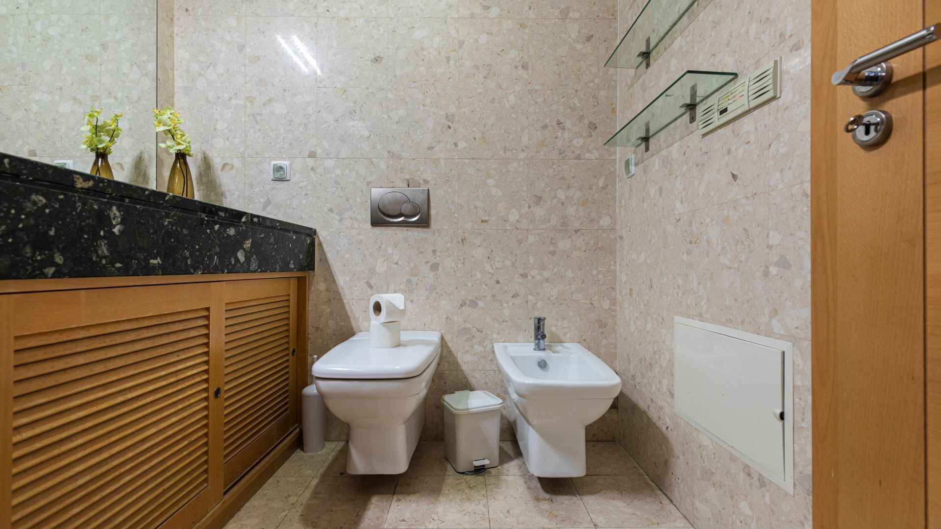 Ein kleines Badezimmer mit einem Holzwaschtisch, zwei Toiletten, einem Bidet und einem Spiegel.